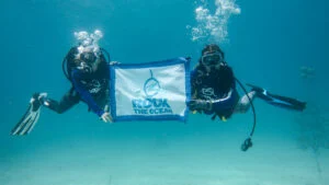 Rock The Reef Volunteers scuba diving holding Rock The Ocean Flag